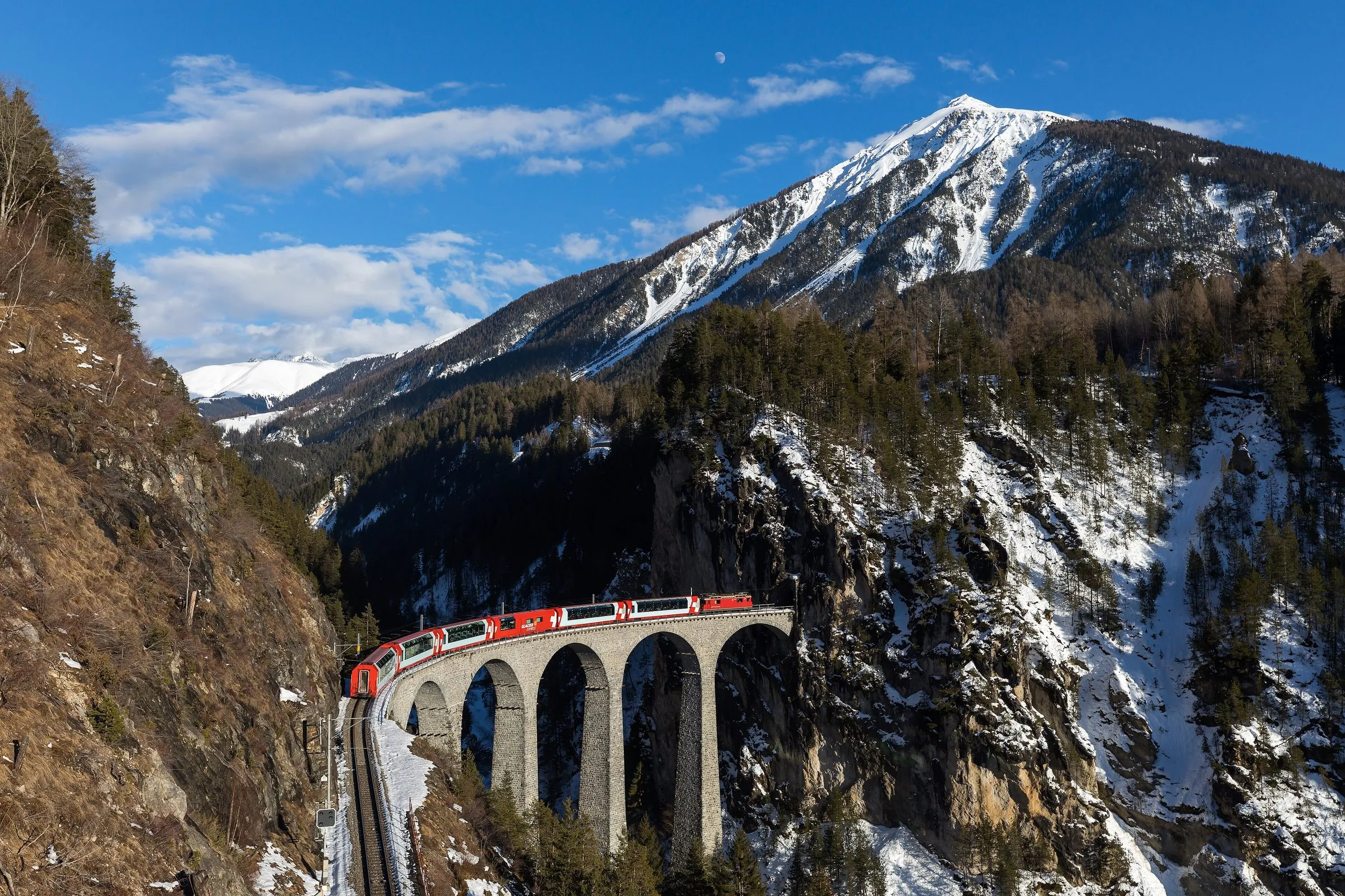 Czerwony pociąg Glacier Express na wiadukcie Landwasser, ośnieżony szczyt w tle